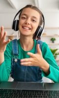 Smiling girl in headset using laptop, talking during videochat
